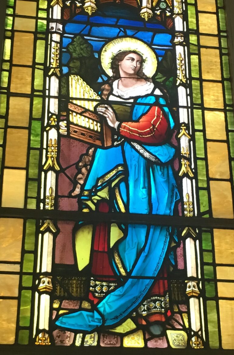 A stained-glass window of a haloed figure holding a book, in green, gold, red and blue