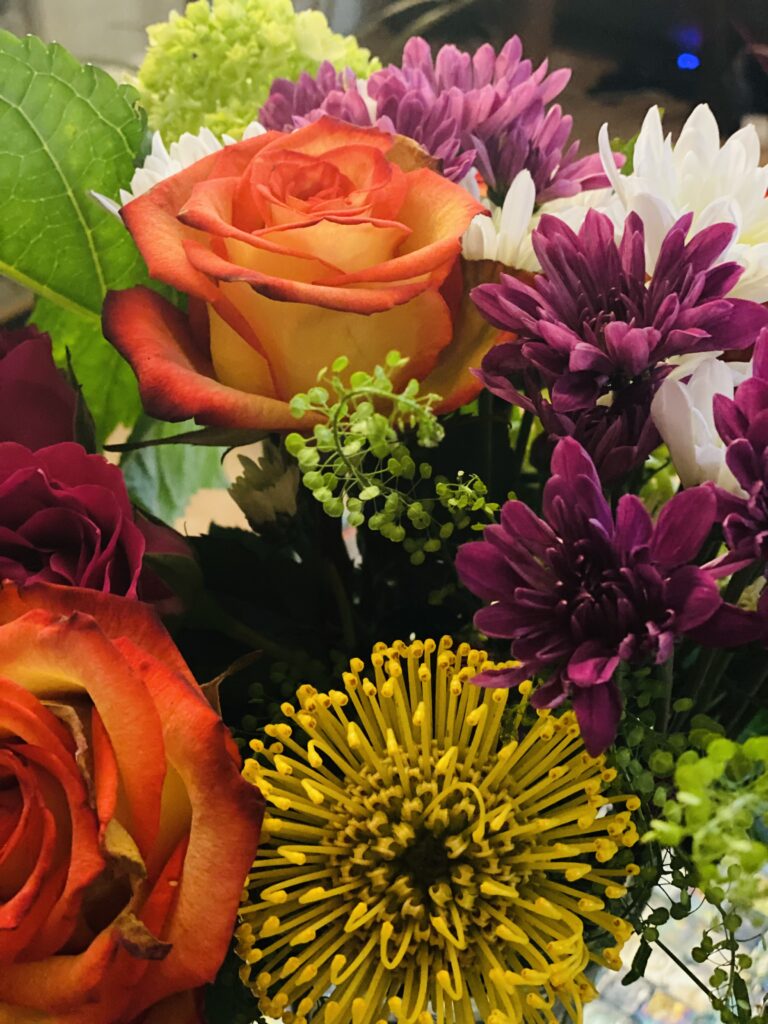 A bouquet of roses, purple chrysanthemums and a yellow pincushion protea
