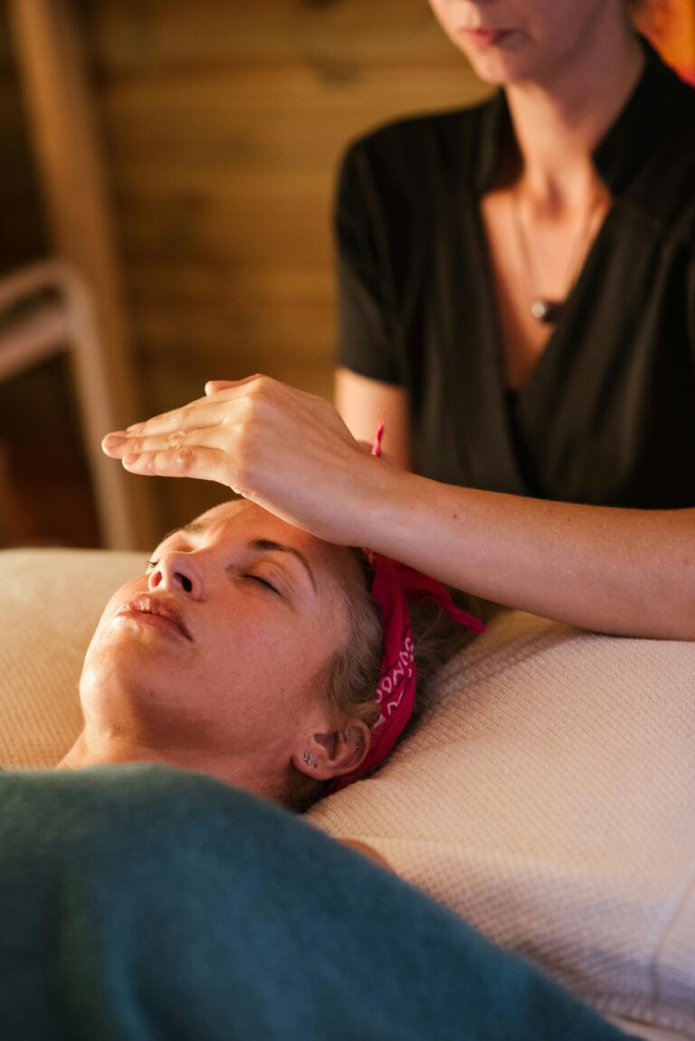 A Reiki practitioner holding her hands gently above a relaxed client's forehead in a warm, calm session room