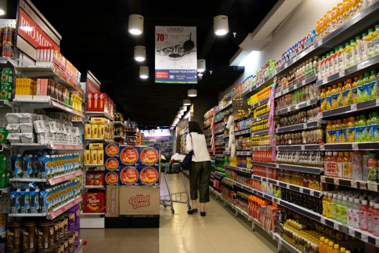 A woman pushing a shopping cart down a brightly lit supermarket aisle, evoking the everyday moment of absorbing strangers' energy in public spaces
